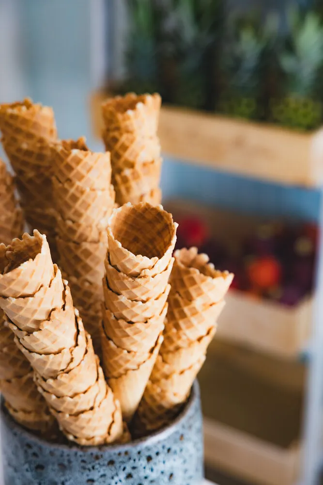 Fresh waffle cones bunched in a stone pot, crates of lemons and pineapples behind.